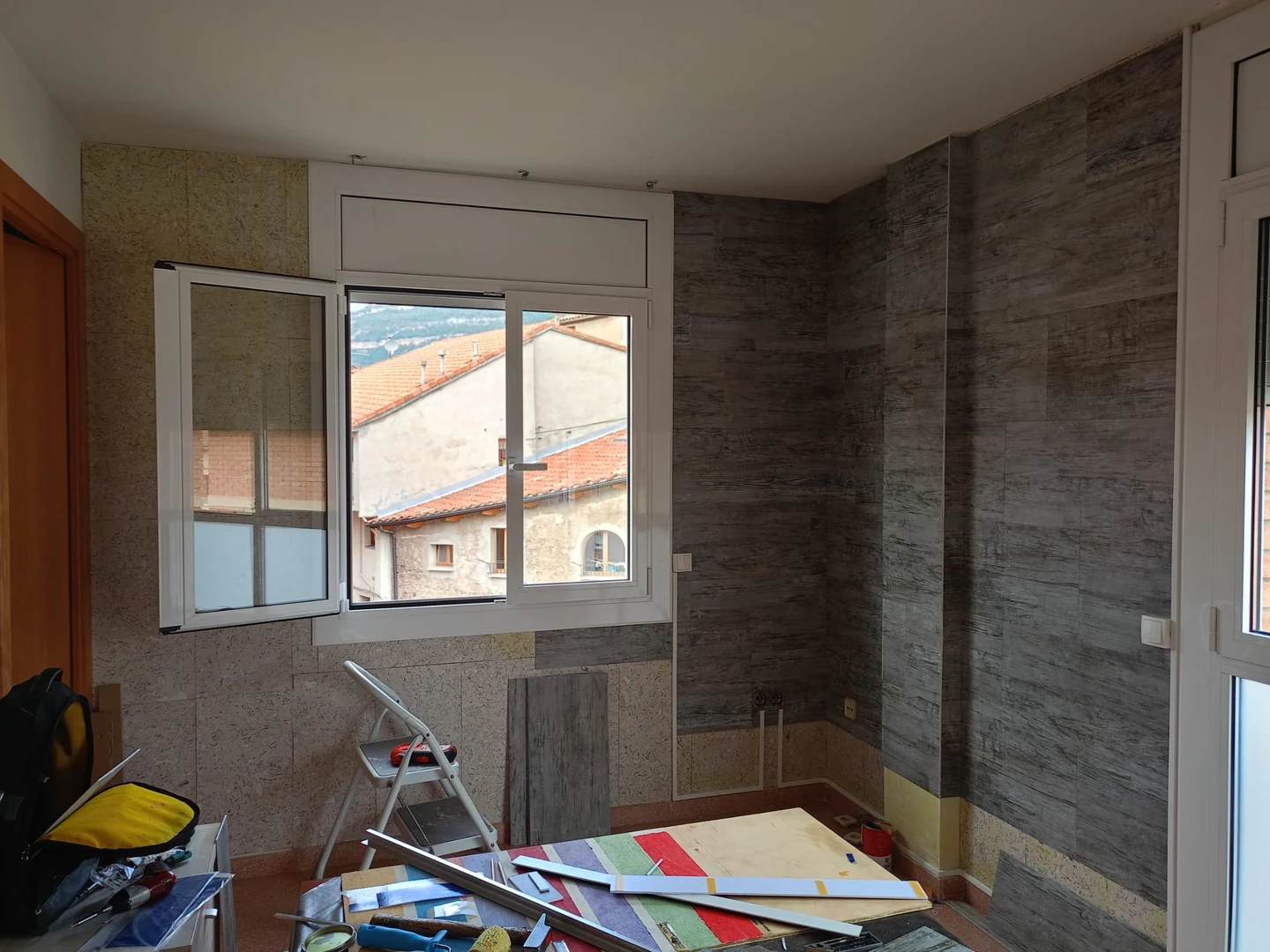 Instalación del revestimiento efecto madera, con zonas inferiores pendientes y herramientas junto a la ventana