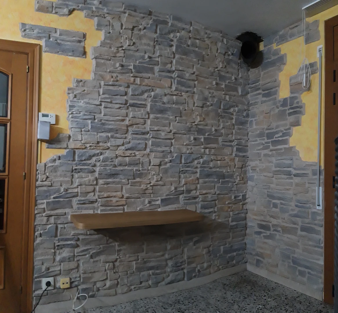 Rincón revestido con piedra gris, juntas rematadas y una balda de madera