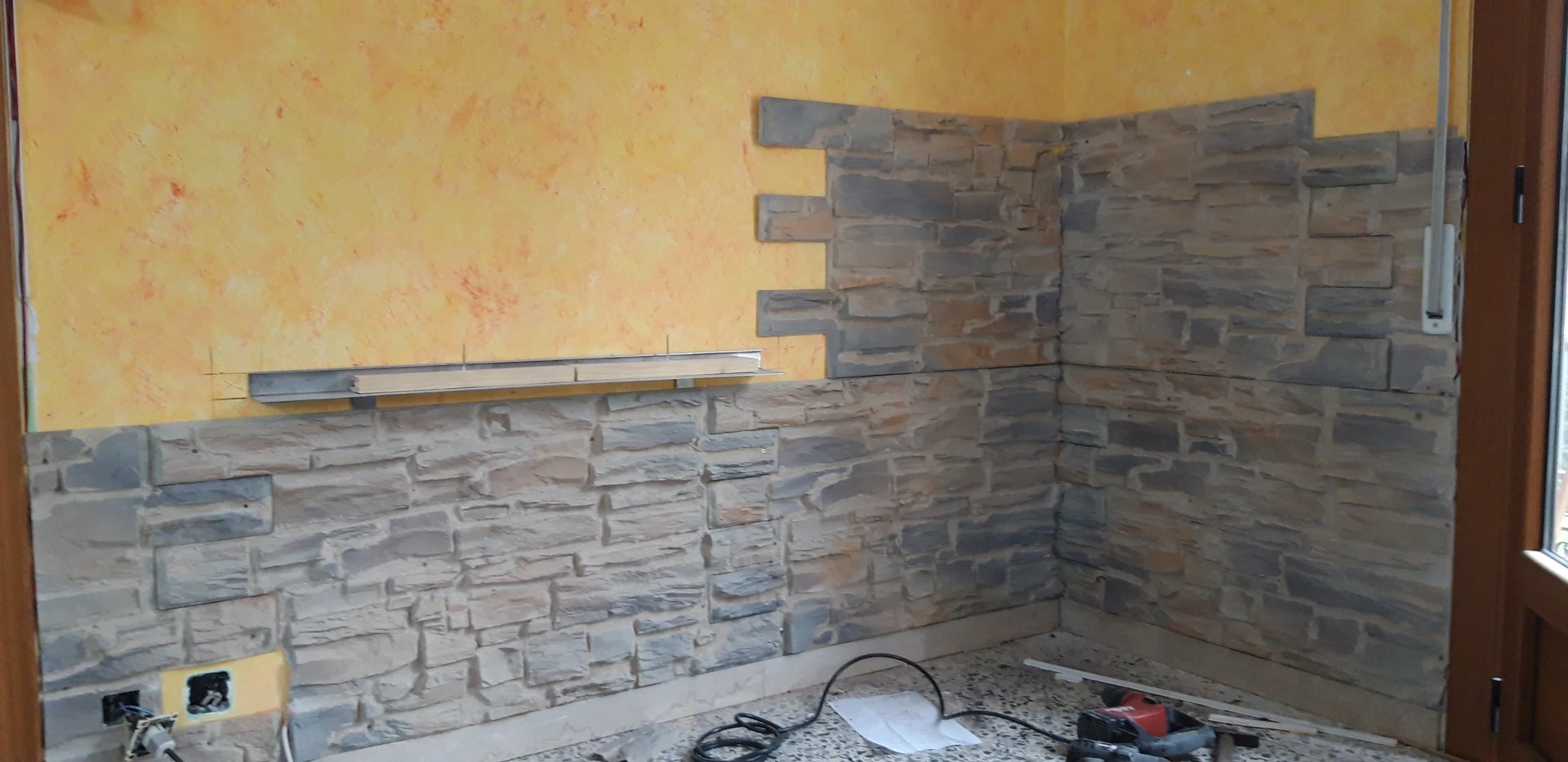 Pared amarilla con la primera parte del revestimiento de piedra gris colocada