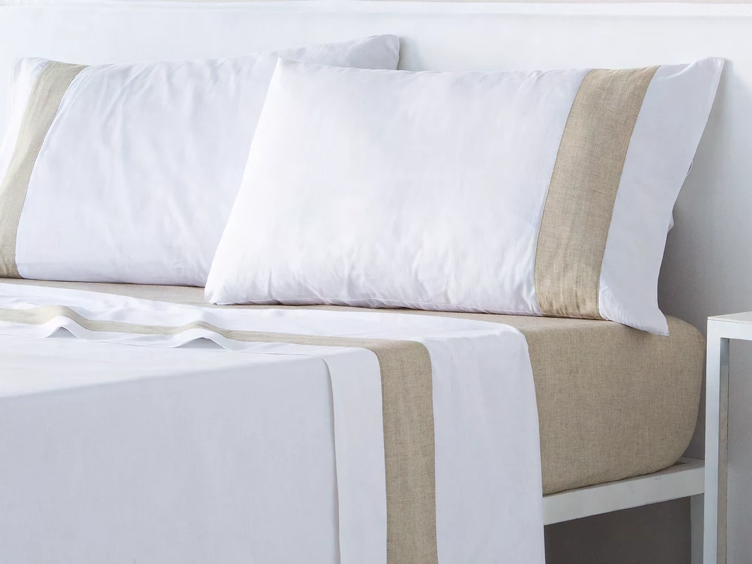 Detalle de sábanas blancas con ribete beis y almohadas sobre una cama, catálogo Fun & Deco